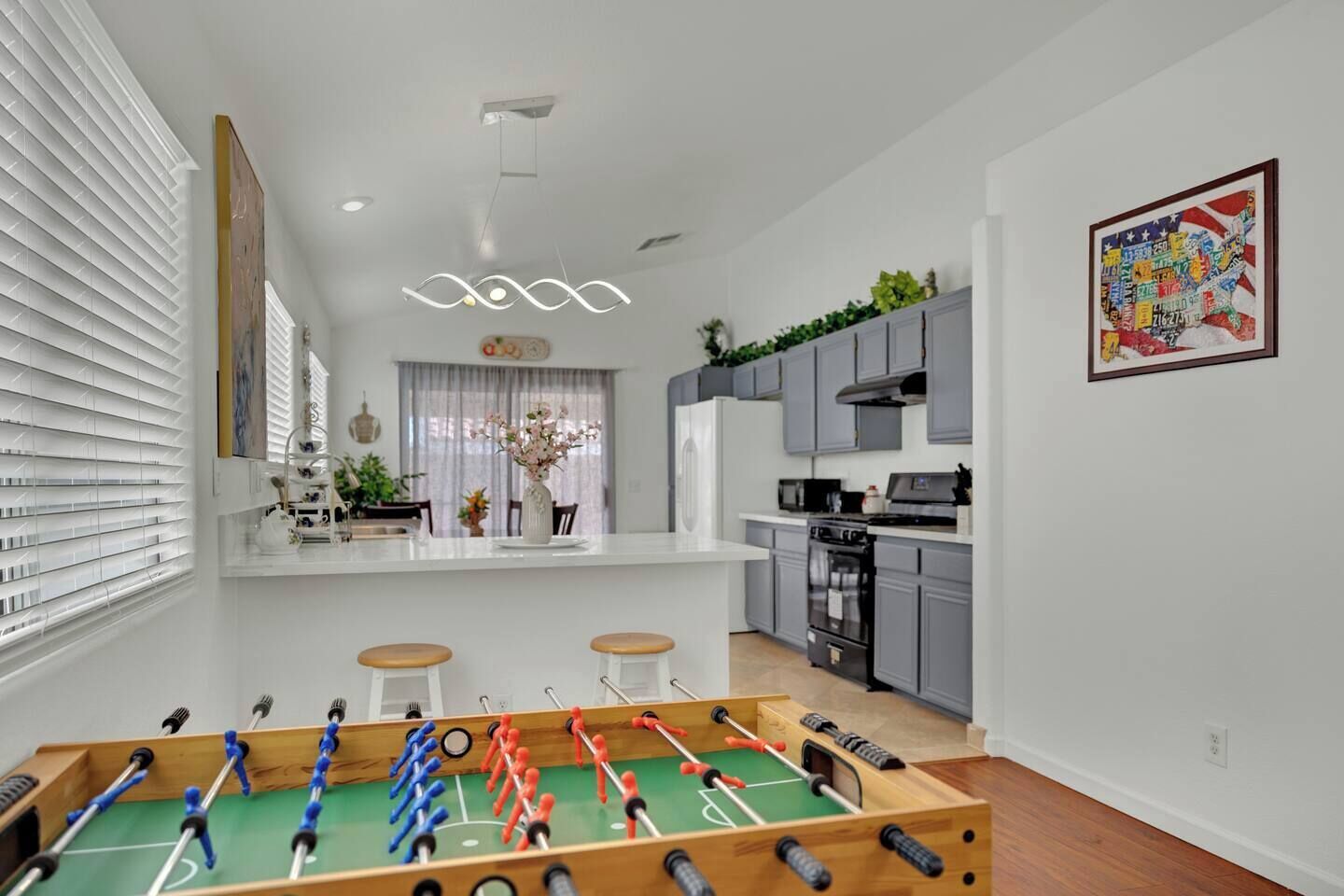 Une cuisine moderne avec des meubles gris, un îlot central et une table de baby-foot au premier plan.
