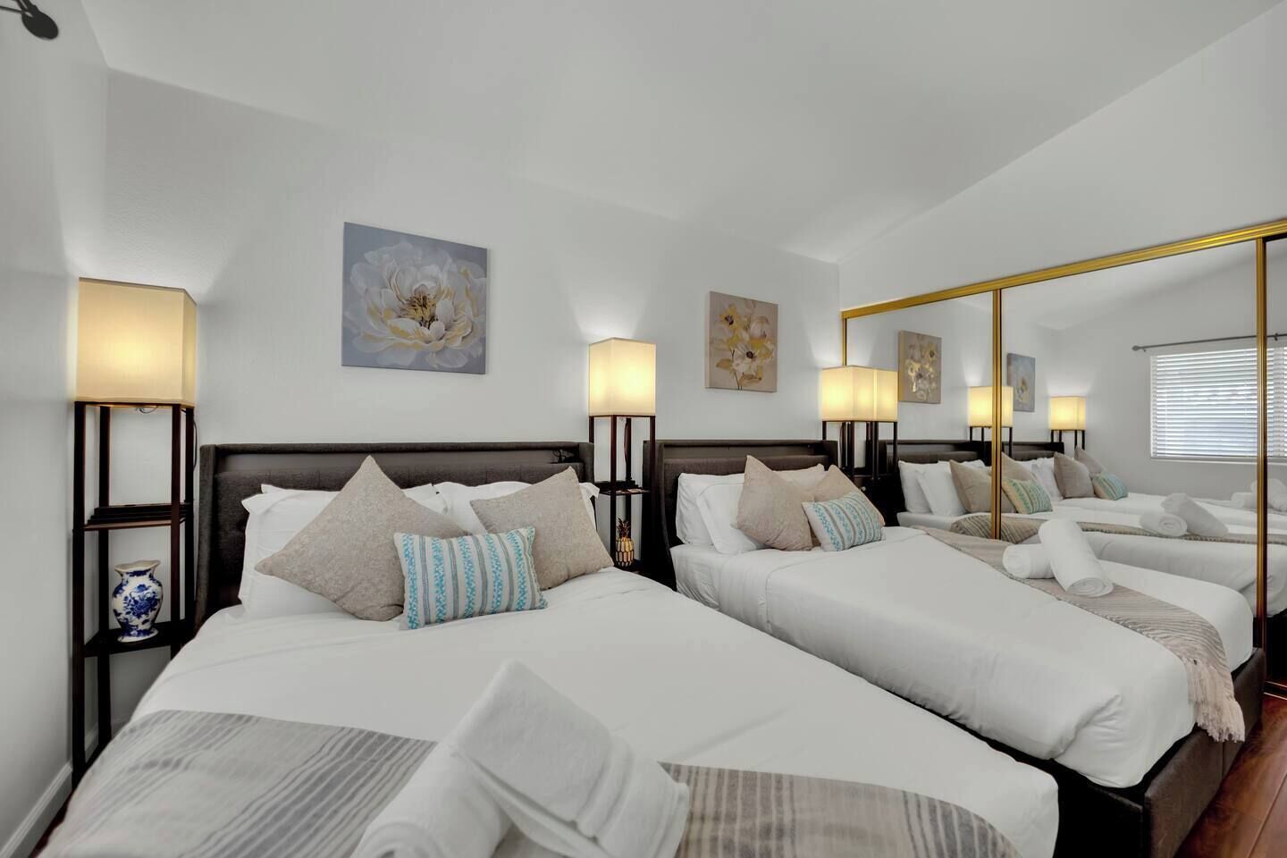 Ein Hotelzimmer mit zwei Betten, jeweils mit Kopfteil, Nachttischlampen und Zierteichen.