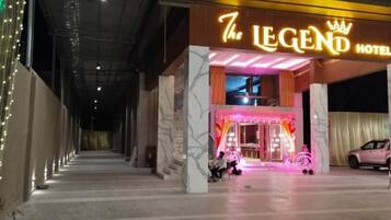 Entrada de hotel con un letrero de neón, un coche estacionado en el interior y una persona sentada en los escalones.