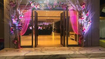 Entrada de hotel con puerta de cristal, suelo de mármol y decoración floral.