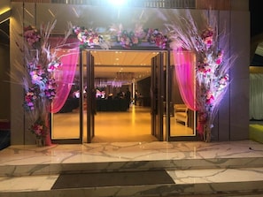Een hotelingang met een glazen deur, een marmeren vloer en bloemdecoraties.