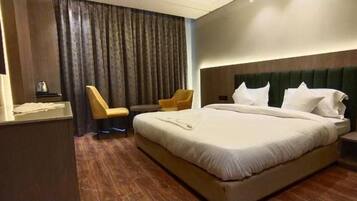 Habitación de hotel con una cama grande, una silla, una mesita y un televisor.