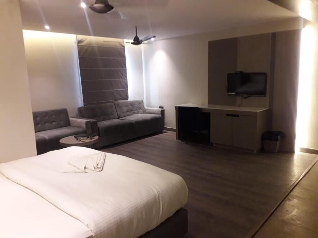 Een moderne hotelkamer met een bed, een bank, een klein tafeltje, een televisie en een plafondventilator.