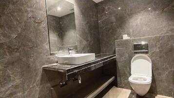 Un baño moderno con pared de mármol, lavamanos blanco y un inodoro.