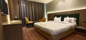 Een hotelkamer met een groot bed, een nachtkastje, een stoel, een televisie en een gordijn.