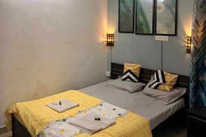 Una cama individual con colcha amarilla, ropa de cama gris y almohadas estampadas. Hay lámparas de pared a ambos lados de la cama.