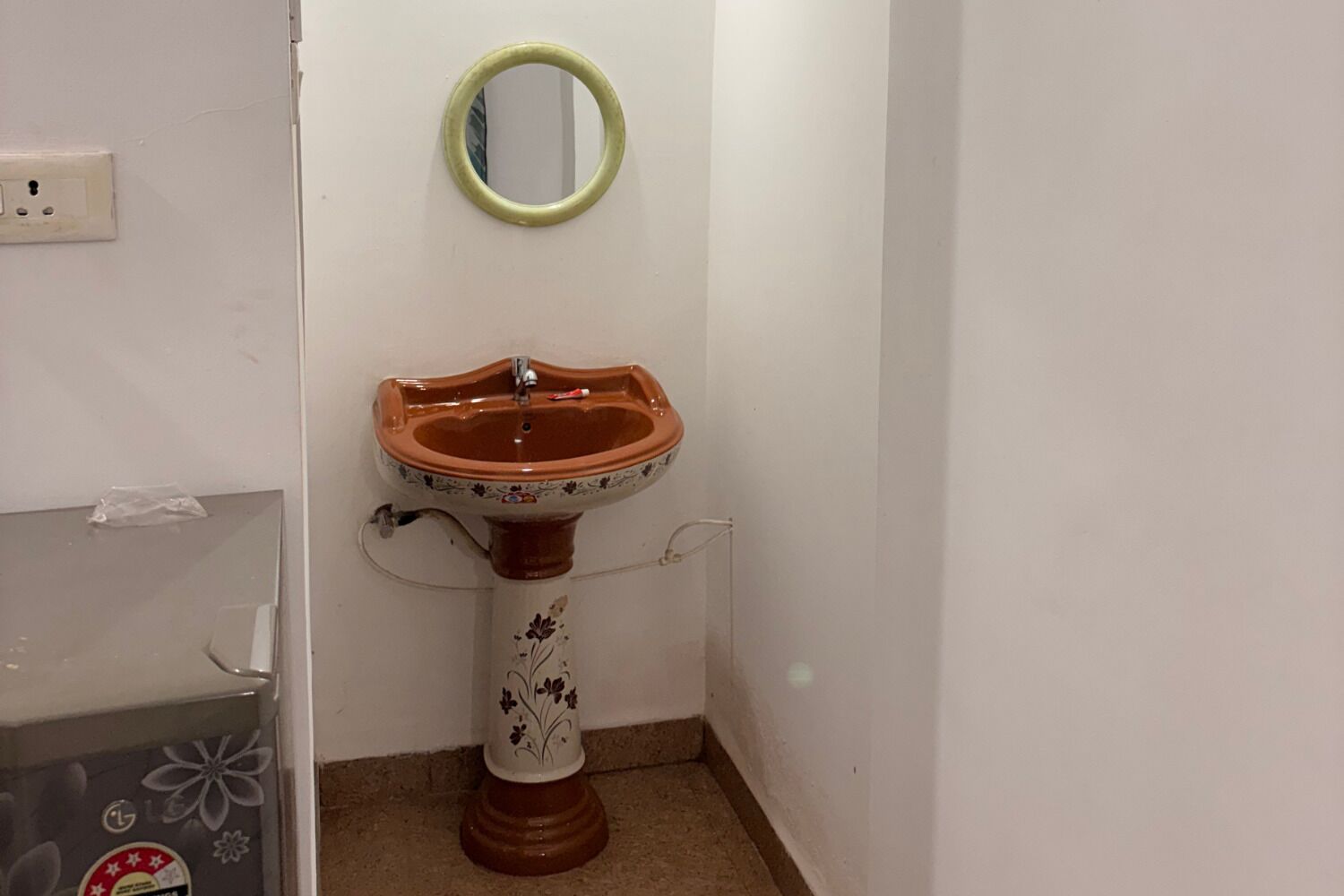 Ein Badezimmer mit einem Waschbecken auf Säule, einem Spiegel und einer Wandsteckdose.