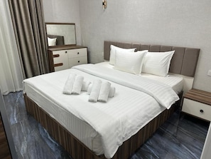 A hotel room with a large bed, a nightstand, a mirror, and a wooden floor. - Yakkasaray Premium Apartment 2 (Tashkent)