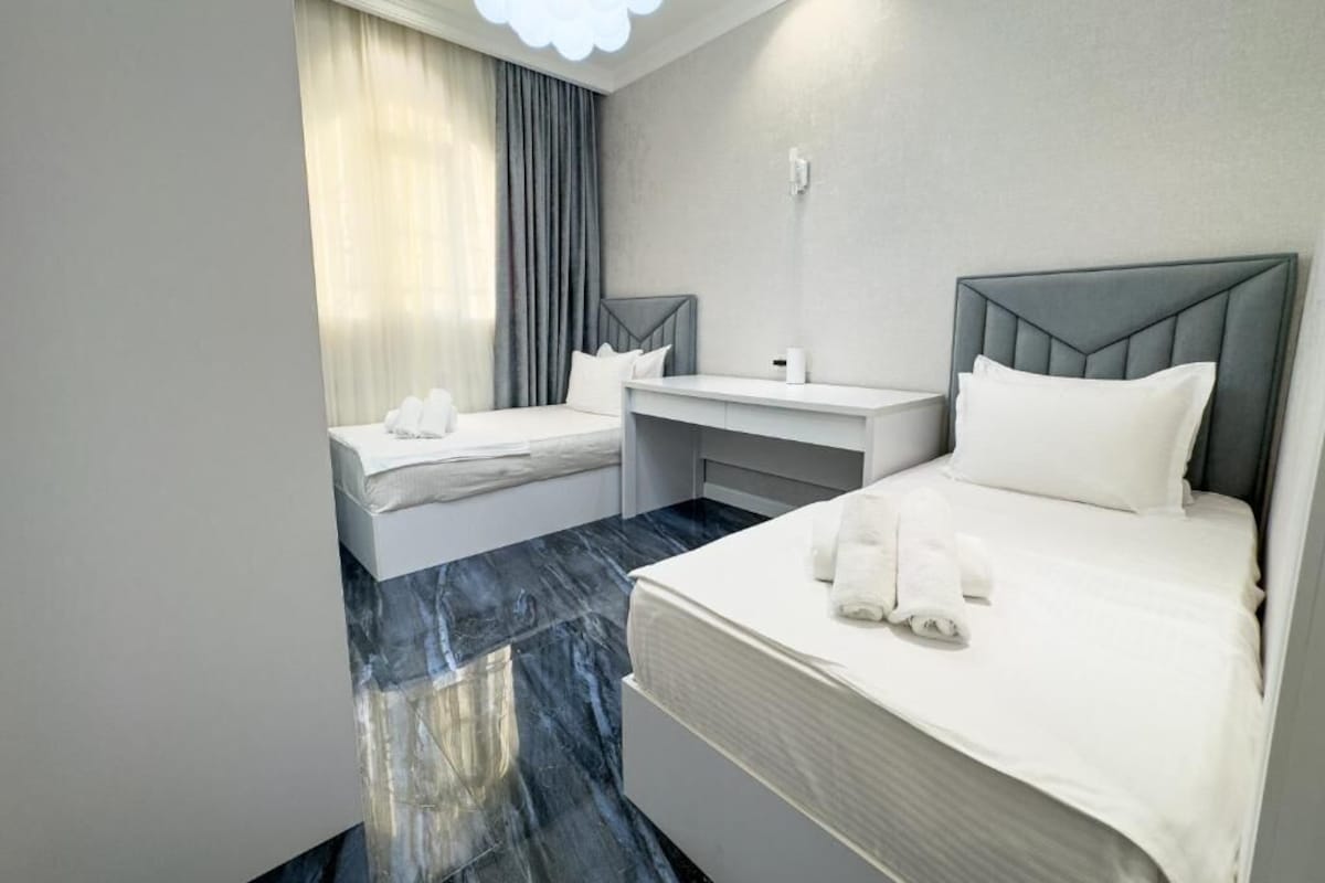 A hotel room with two beds, a desk, and a large window with curtains.