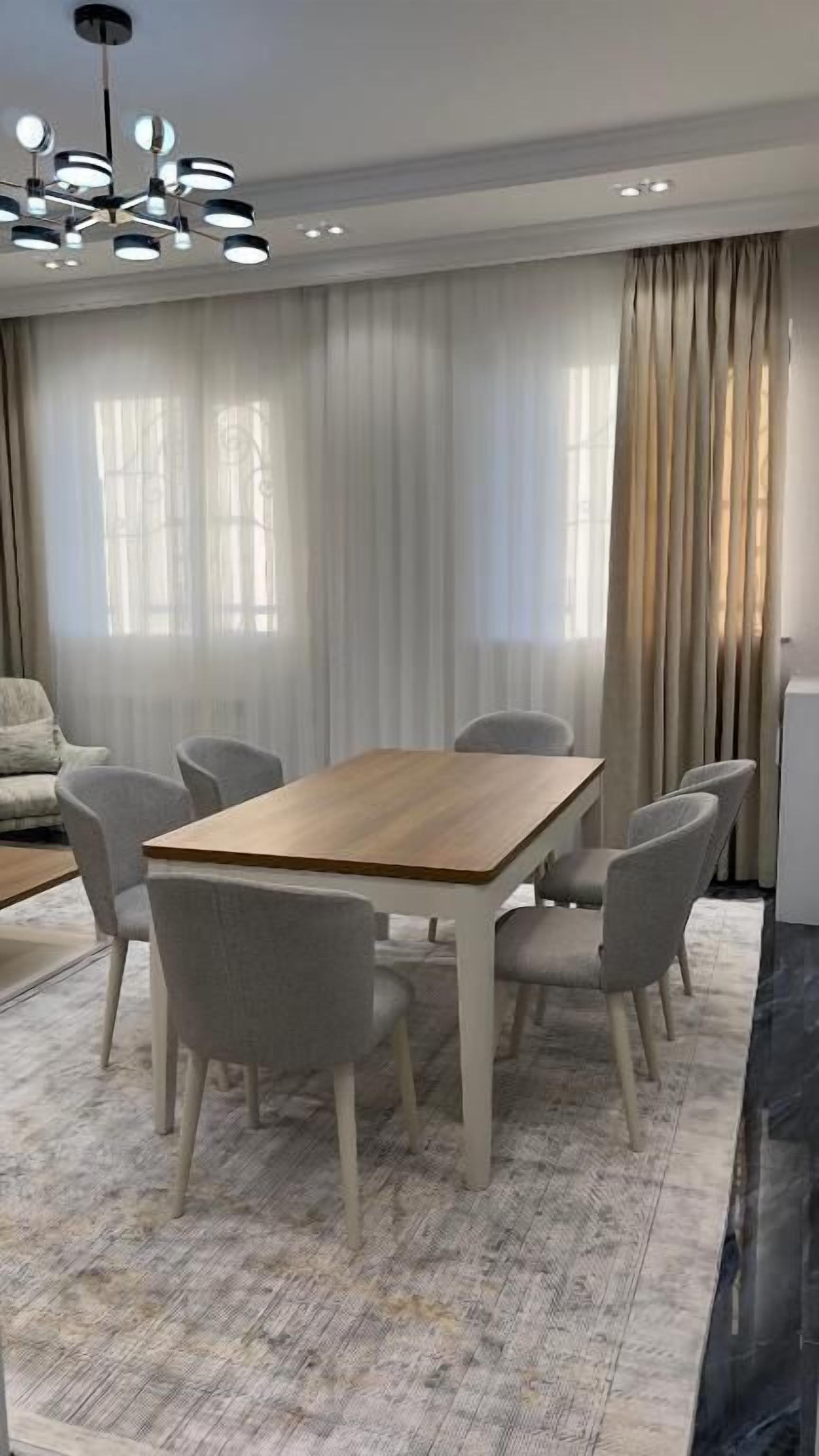 A dining area with a wooden table and six chairs, a sofa, and a chandelier.