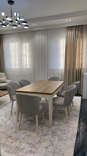 A dining area with a wooden table and six chairs, a sofa, and a chandelier. - Yakkasaray Premium Apartment 2 (Tashkent)