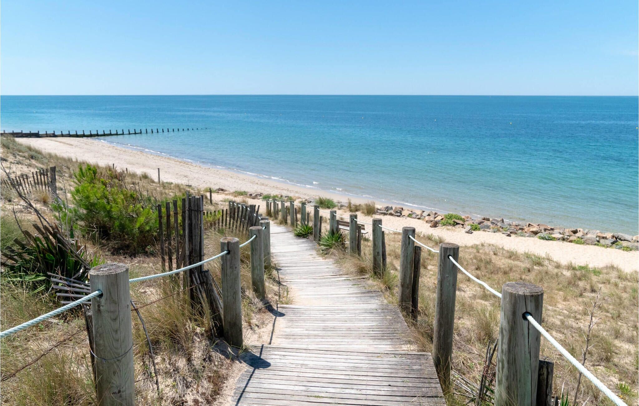 A wooden boardwalk leading to a beach with a clear view of the ocean.