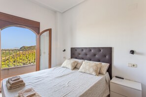 Ein Schlafzimmer mit Bett, Nachttisch, einer Steckdose und einem Fenster mit Blick auf Grünflächen.