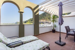 Un balcon avec vue sur une colline, une plante en pot et un parasol de patio.