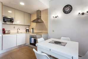 A modern kitchen with white cabinets, a microwave, a stove, and a sink. There is a dining table with chairs and a clock on the wall. - Apartment 'Casa De Panorama' with Lake View, Wi-Fi and Air Conditioning (Xeresa)