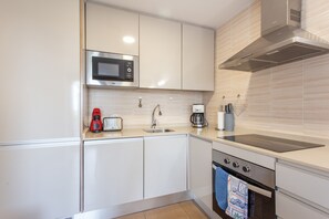 Une cuisine moderne avec des meubles blancs, un four à micro-ondes en acier inoxydable, une machine à café et une cuisinière à gaz.