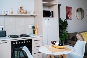 Eine kompakte Küche mit Herd, Backofen und Mikrowelle. Es gibt eine Essecke mit Tisch und Stühlen sowie eine Couch im Hintergrund.