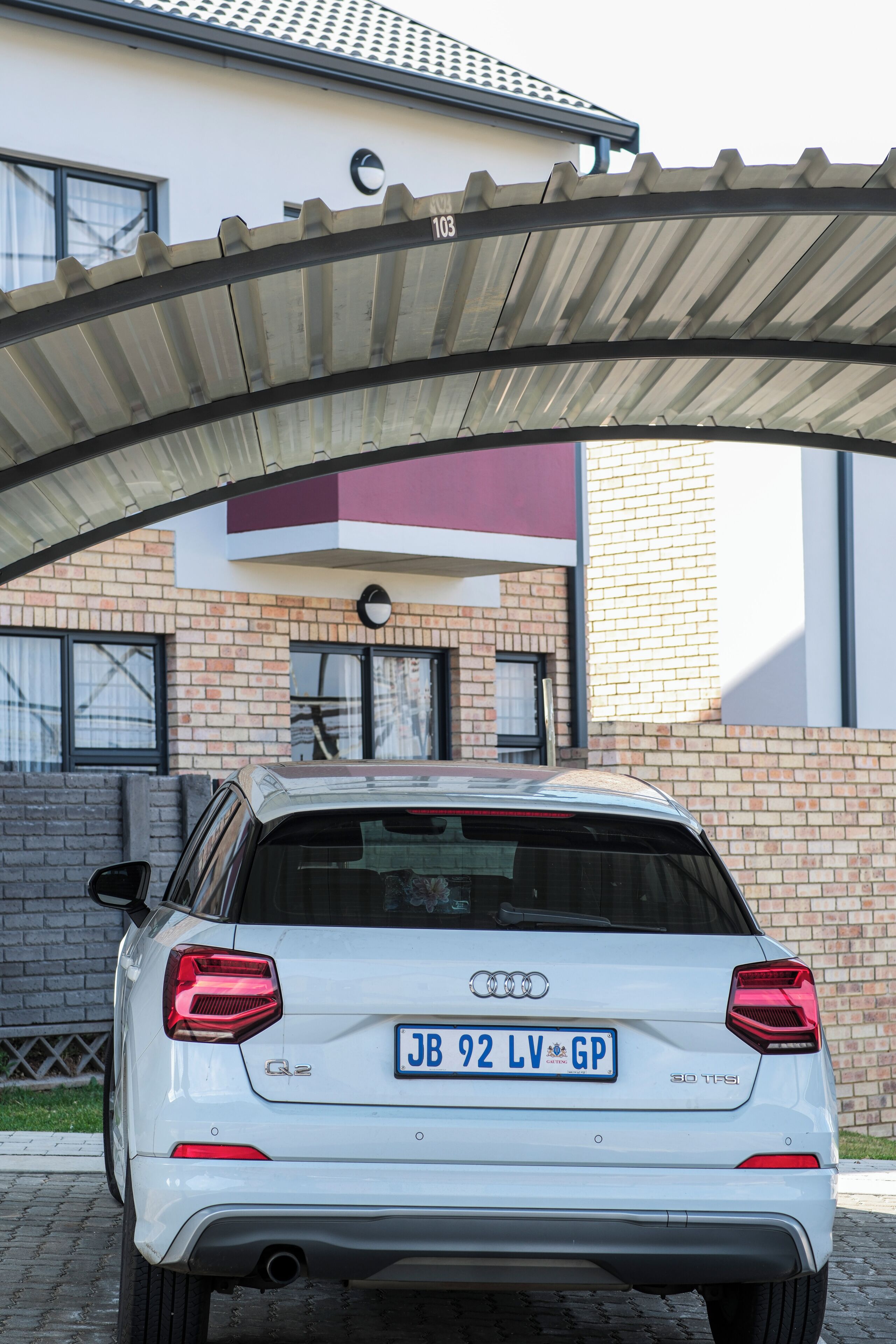 Une Audi Q2 blanche est garée sous un abri, avec un bâtiment en briques en arrière-plan.