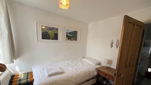 Quarto com uma cama de solteiro, porta de madeira, mesa de cabeceira com abajur e duas fotos emolduradas na parede.