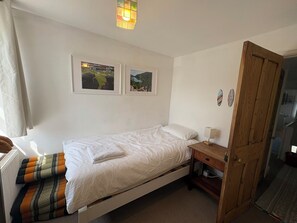 Et enkeltværelse med en trædør, et natbord med lampe og to billeder i rammer på væggen.