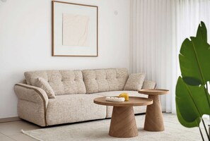 A neutral-toned living room with a sofa, two round wooden side tables, a framed artwork, and a large green plant. - Cozy & Spacious 3BR  with Balcony & Mamad (Bat Yam)