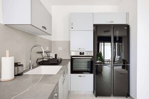 A modern kitchen with a built-in oven, a stainless steel range hood, and a black refrigerator. - Cozy & Spacious 3BR  with Balcony & Mamad (Bat Yam)