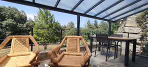 A covered outdoor seating area with two wicker chairs and a table, overlooking a rocky landscape and trees. - Gite du Petit Bois: a quiet spot where you can enjoy the sounds of cicadas and birdsong (Gravières)