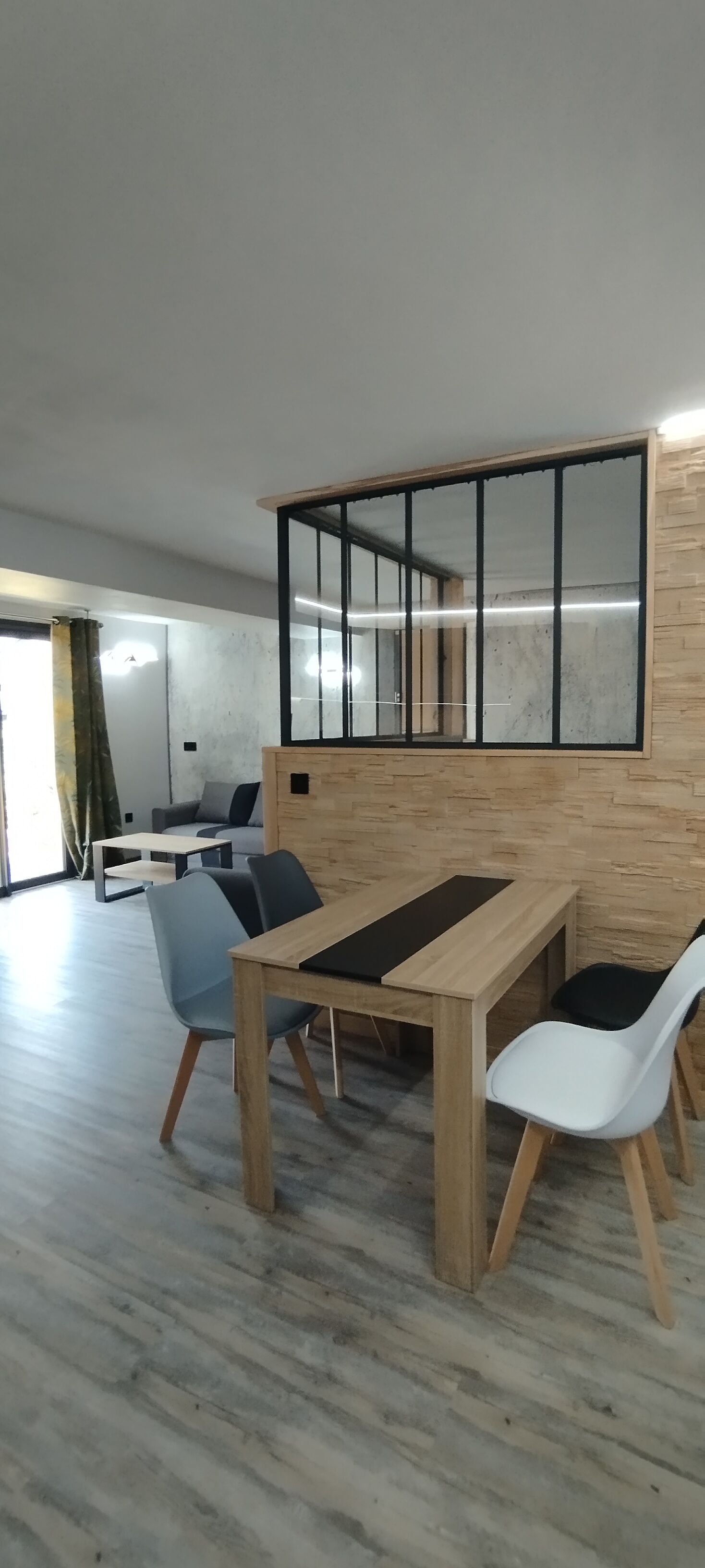 A modern interior with a wooden dining table, chairs, and a large window with blinds.