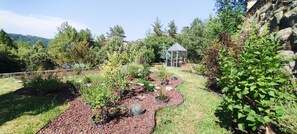 A garden with a greenhouse, various plants, and a stone wall. - Gite du Petit Bois: a peaceful place to enjoy the sound of cicadas and birdsong (Gravières)