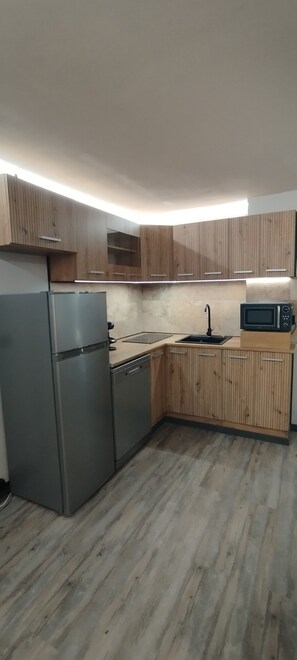 Una cocina compacta con armarios de madera, un refrigerador de acero inoxidable, un microondas y un lavamanos.