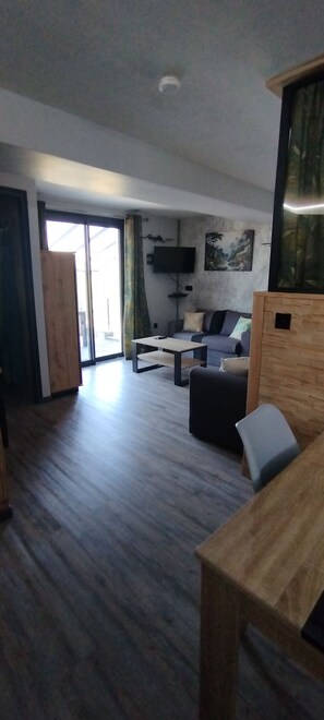 A modern living room with a sofa, a coffee table, and a TV mounted on the wall. - Gite du Petit Bois: a quiet spot where you can enjoy the sounds of cicadas and birdsong (Gravières)