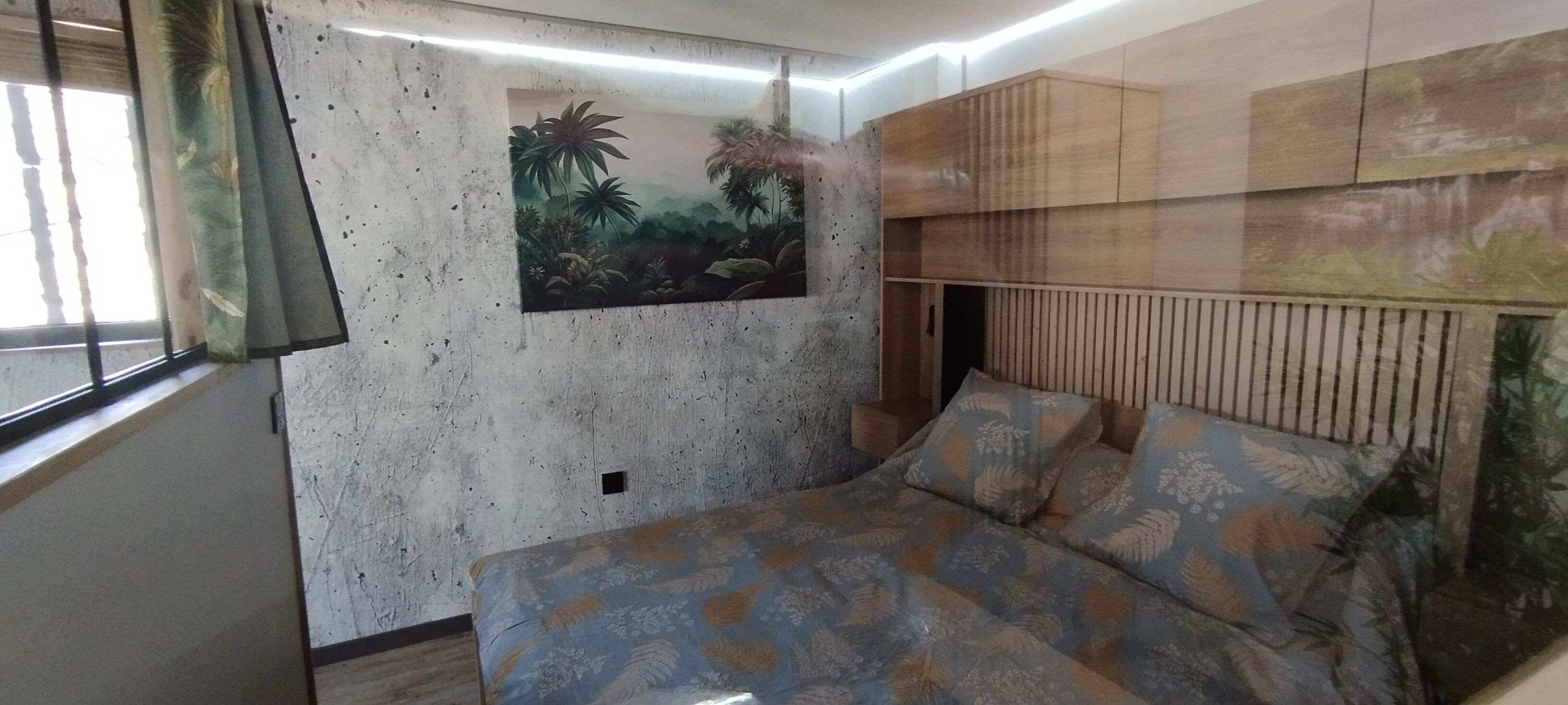 Une pièce avec un lit, une étagère fixée au mur et une fenêtre avec des rideaux.