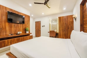 Een slaapkamer met een groot bed, een houten kledingkast, een aan de muur bevestigde televisie, een bureau met een stoel en een plafondventilator.