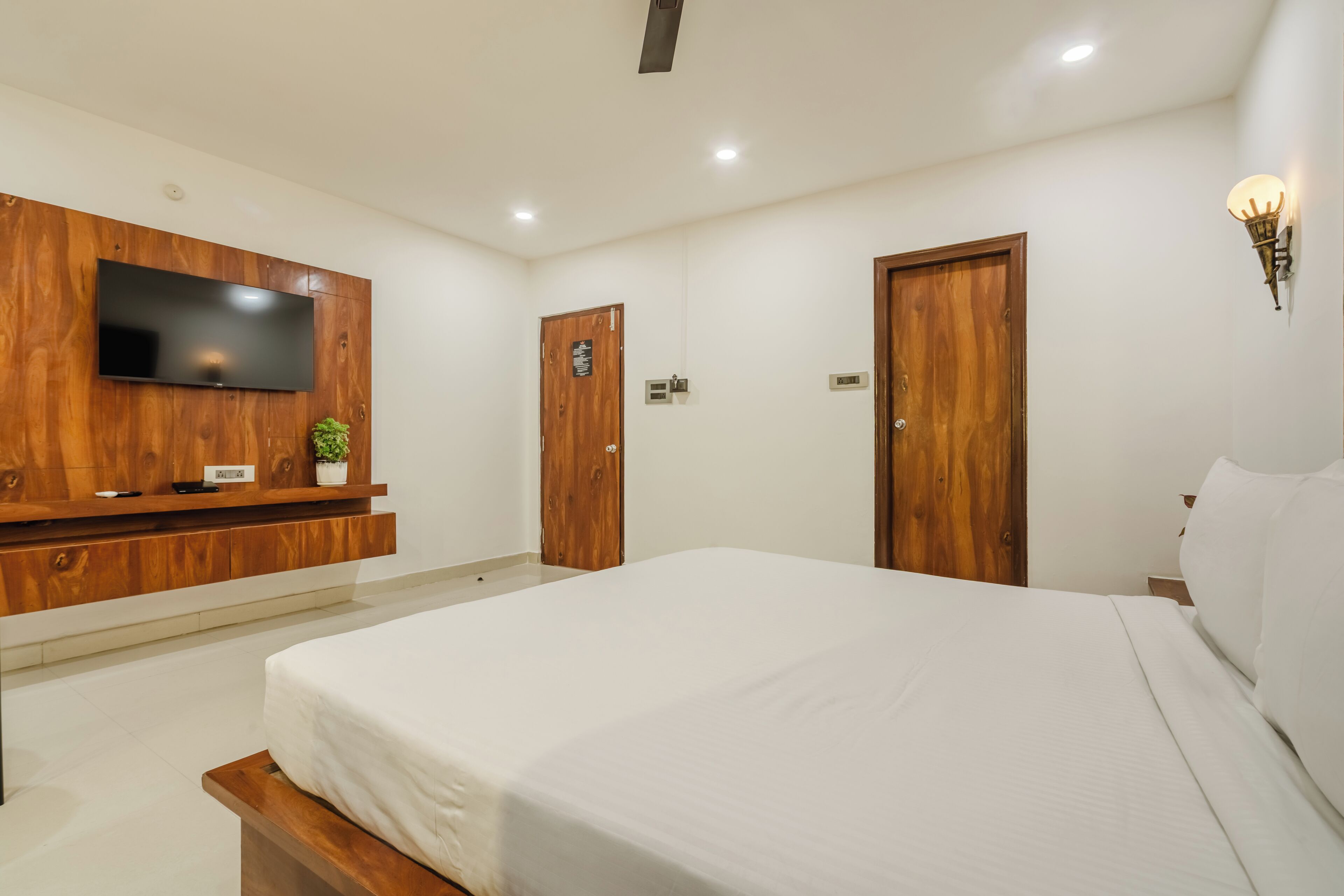 Un dormitorio con una cama grande, un armario de madera, un televisor de pantalla plana y una lámpara fijada a la pared.