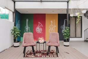 Un balcón con dos sillas rosadas, una pequeña mesa con una cesta, y una pared colorida decorada con instrumentos musicales.