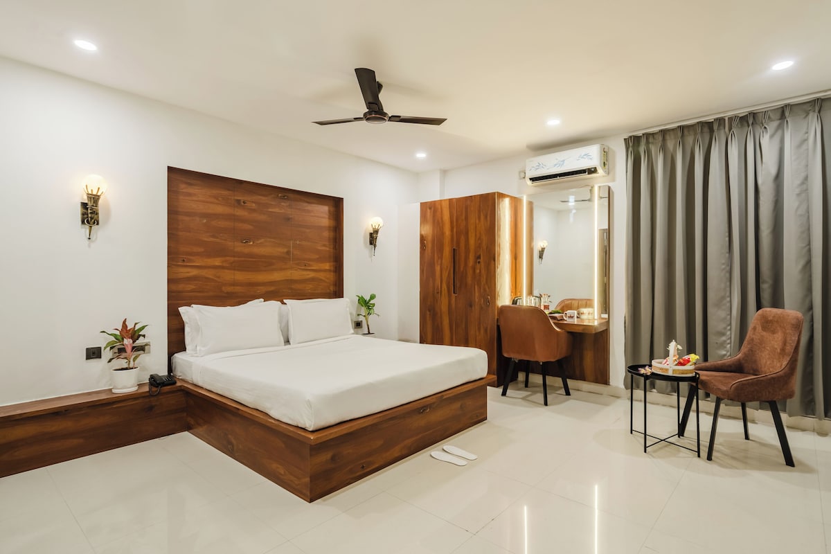 Een moderne hotelkamer met een houten hoofdeinde, een bed, een bureau met stoel, en een kleine tafel met stoel.