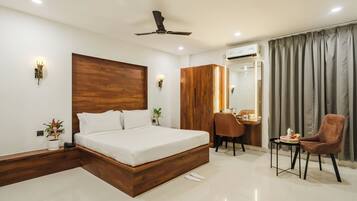 Una habitación de hotel moderna con cabecera de madera, cama, escritorio con silla y una pequeña mesa con otra silla.