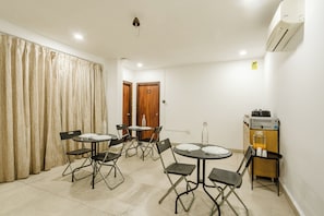 Een hotelkamer met twee tafels, vier stoelen, een minibar en een deur met een nummer.