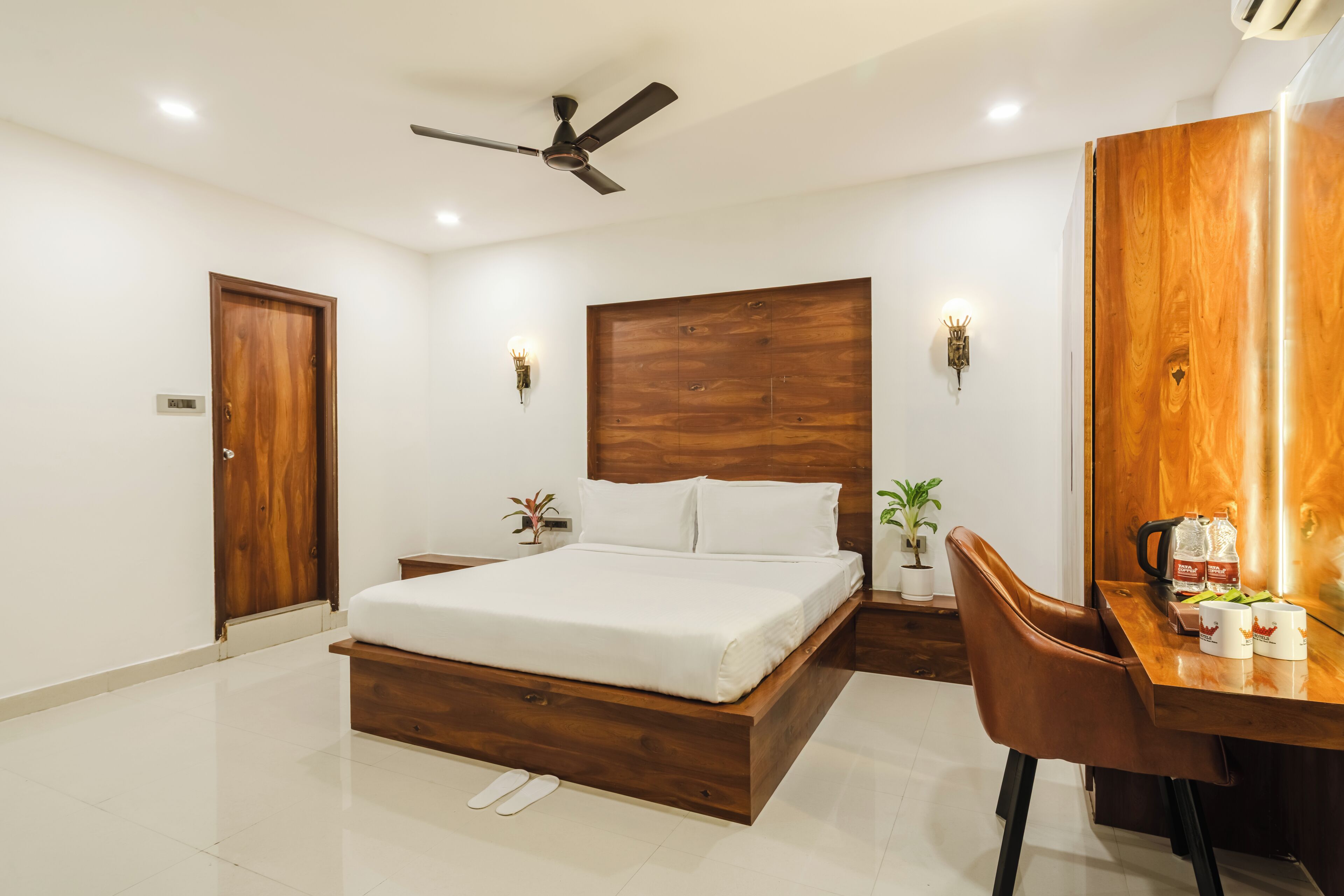 Un dormitorio moderno con estructura de cama de madera, un escritorio con silla, ventilador de techo e iluminación instalada en la pared.