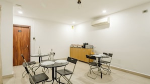 A conference room with a wooden door, a white air conditioning unit, a cabinet with kitchen appliances, and foldable chairs.