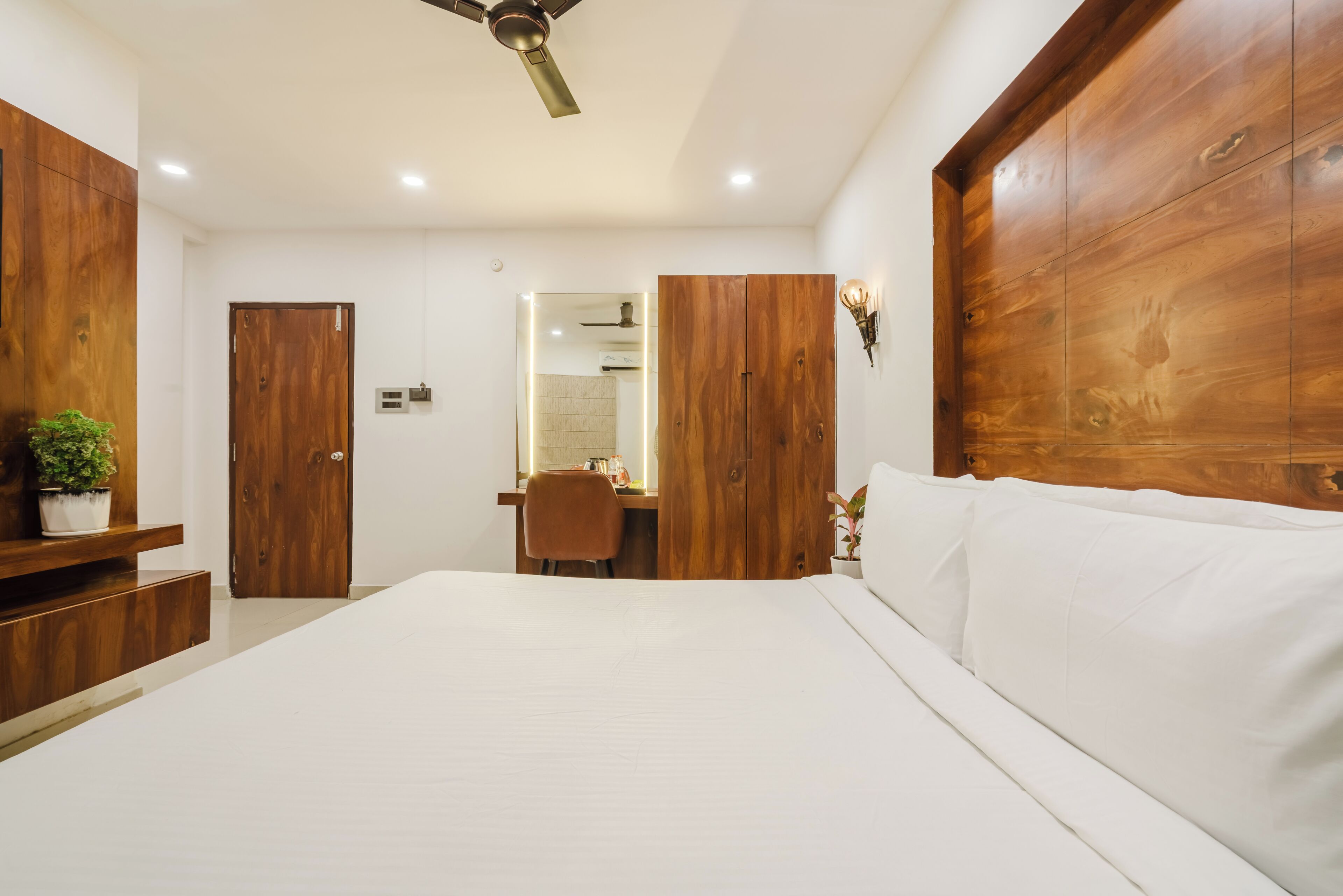 A bedroom with a large bed, wooden wardrobe, and a desk with a chair.