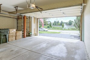 Een open garage met een betonnen vloer, een groene kruiwagen en een ladder die tegen de muur staat.