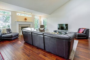 Ein Wohnzimmer mit Ecksofa, Kamin, Fernseher und einem großen Fenster mit Jalousien.