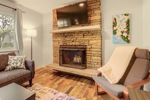A living room with a stone fireplace, a sofa, a chair, and a floor lamp. - The Sugar Shack - Central Loveland Home w/ Patio (Loveland)