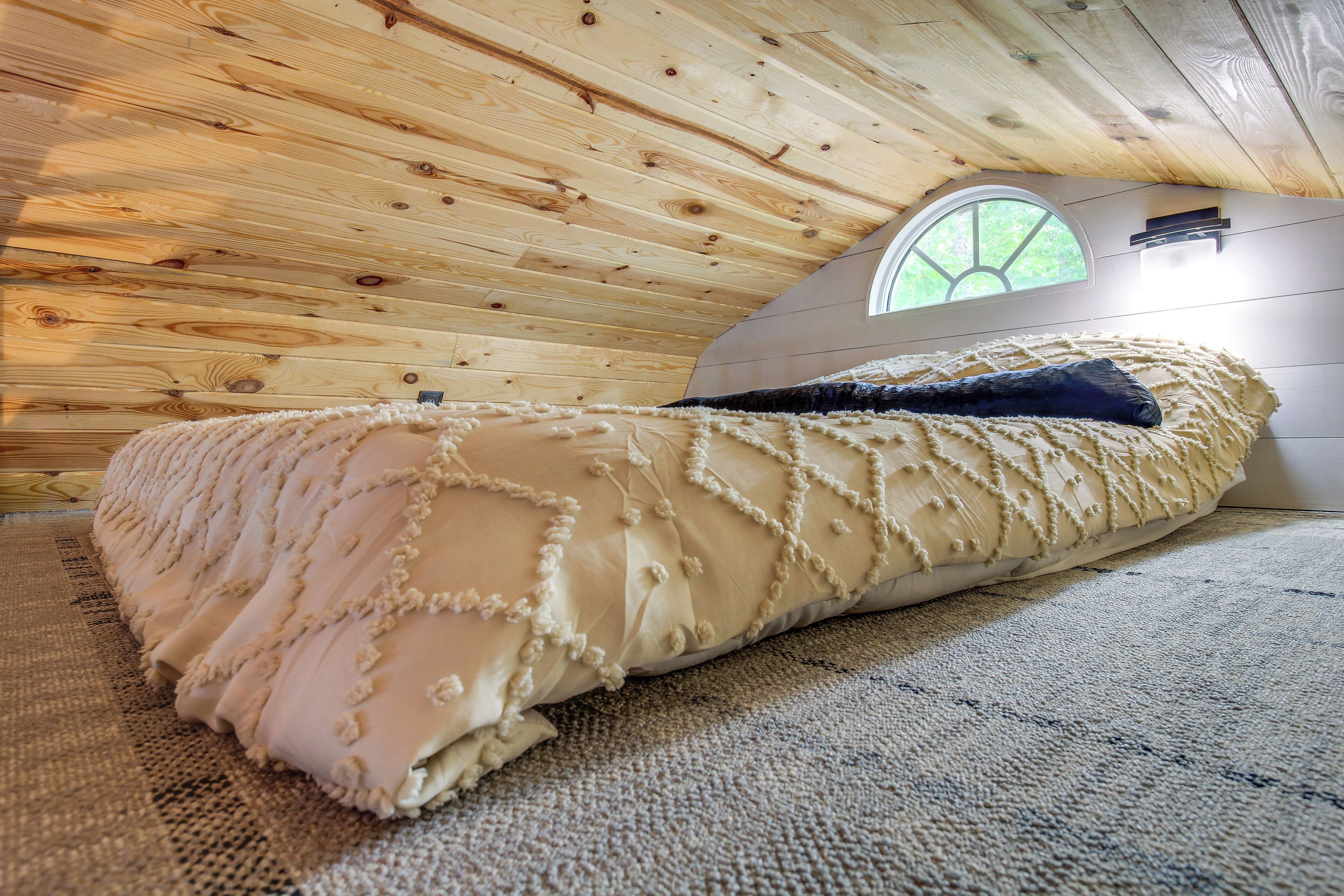 A cozy room with a wooden ceiling, a large window, and a bed with a beige and blue blanket.