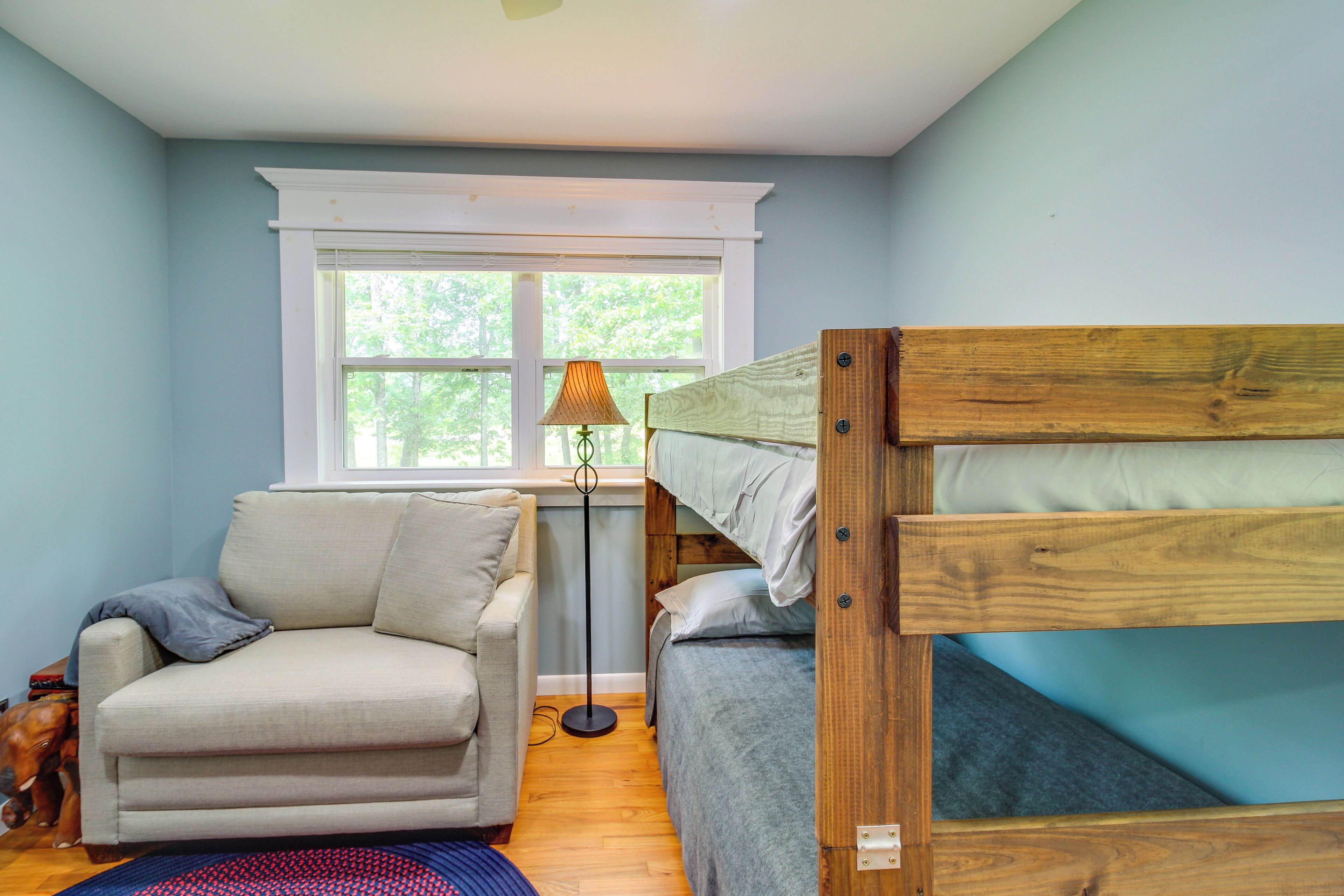 A room with a bunk bed, a sofa, a lamp, and a dog.