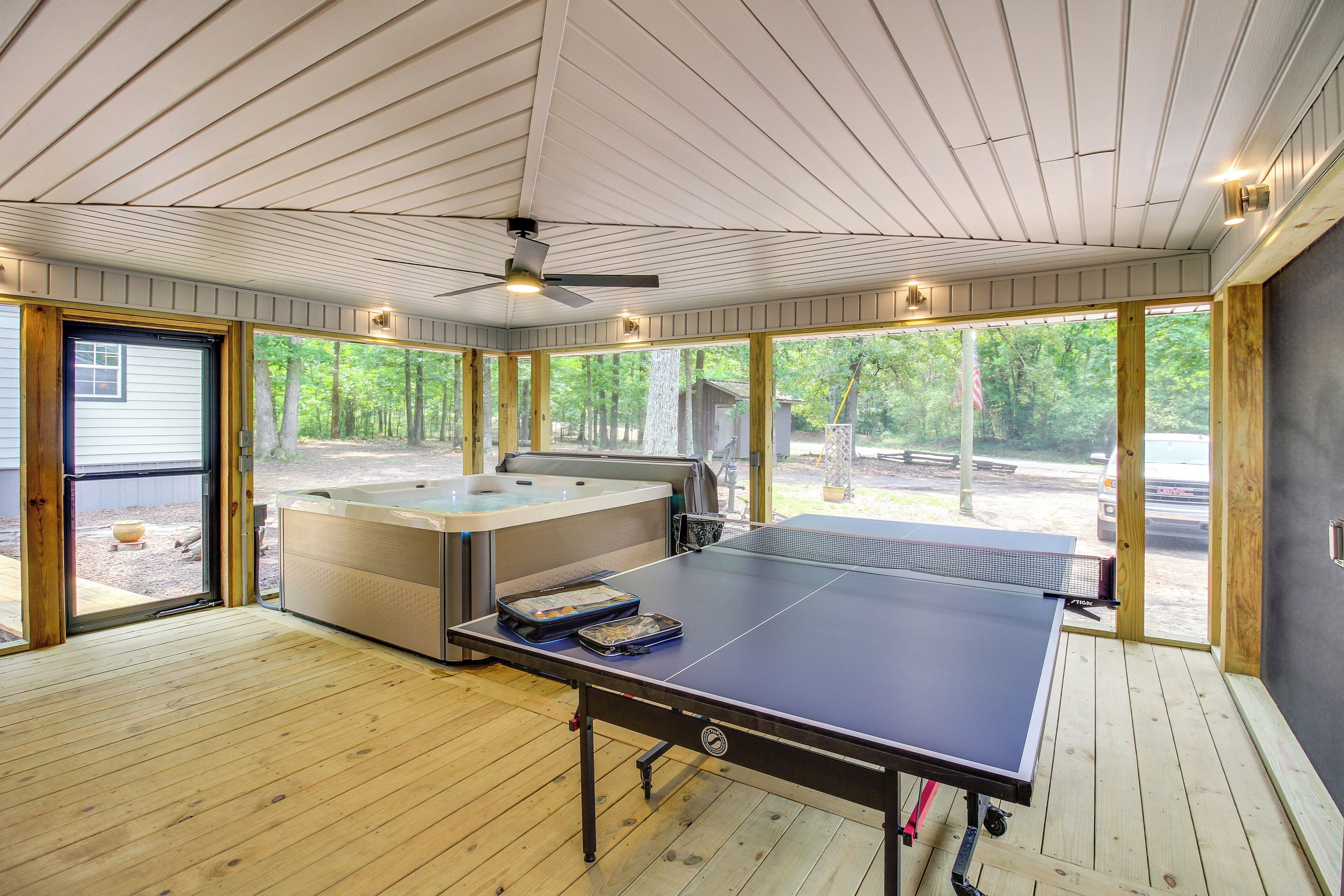 A room with a ping pong table, a hot tub, and large windows offering a view of the outdoors.