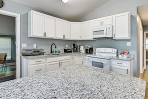 A modern kitchen with white cabinets, a granite countertop, a microwave, a coffee maker, and a stove. - Centrally Located Charlotte Home w/ Patio & Yard! (Charlotte)