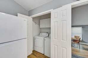 A laundry room with a washing machine and dryer, a white refrigerator, and a dining area with a table and chairs. - Centrally Located Charlotte Home w/ Patio & Yard! (Charlotte)