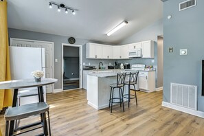 A modern kitchen with white cabinets, a central island with bar stools, a microwave, and a coffee machine. - Centrally Located Charlotte Home w/ Patio & Yard! (Charlotte)